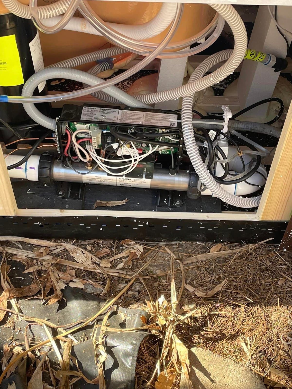 A hot tub equipment bay with control pack, heater, and plumbing
